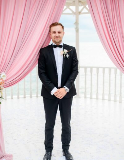 Groom stands alone under the tent for wedding ceremony by the sea
